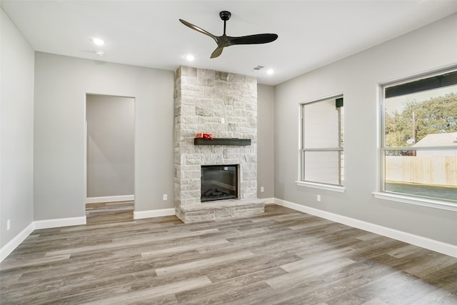 unfurnished living room featuring a stone fireplace, ceiling fan, and wood-type flooring