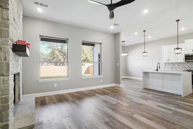 unfurnished living room featuring a fireplace, ceiling fan, sink, and light wood-type flooring