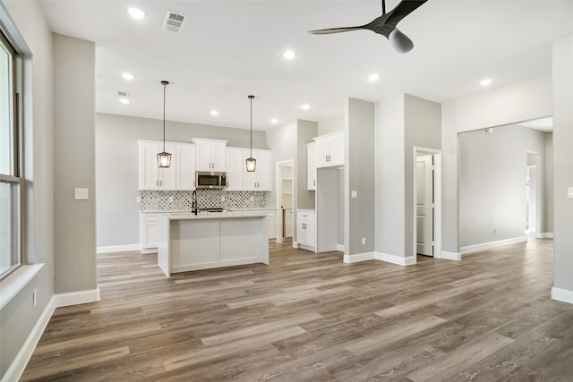 kitchen featuring light wood-type flooring, decorative light fixtures, white cabinetry, plenty of natural light, and an island with sink