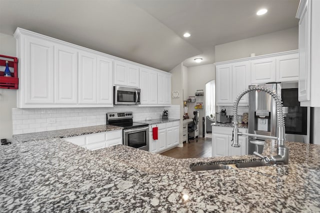 kitchen featuring tasteful backsplash, light stone counters, stainless steel appliances, white cabinets, and lofted ceiling