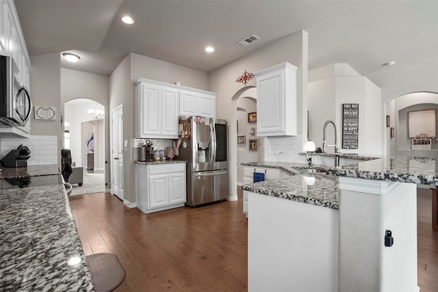 kitchen featuring backsplash, dark stone counters, kitchen peninsula, white cabinetry, and stainless steel appliances