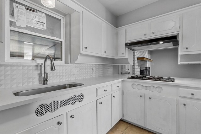 kitchen featuring sink, light tile patterned floors, tasteful backsplash, white cabinetry, and stainless steel gas cooktop