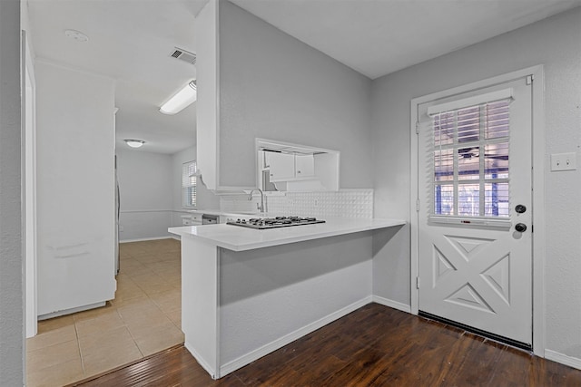 kitchen featuring decorative backsplash, kitchen peninsula, dark hardwood / wood-style flooring, stainless steel gas cooktop, and sink