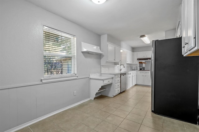 kitchen with appliances with stainless steel finishes, sink, light tile patterned floors, white cabinets, and range hood