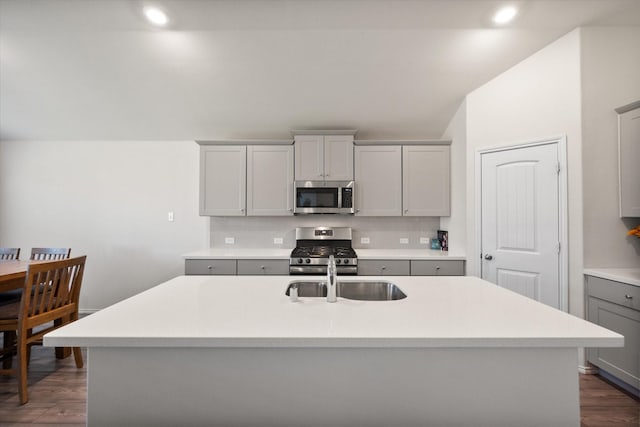 kitchen with appliances with stainless steel finishes, dark hardwood / wood-style flooring, gray cabinetry, sink, and a center island with sink