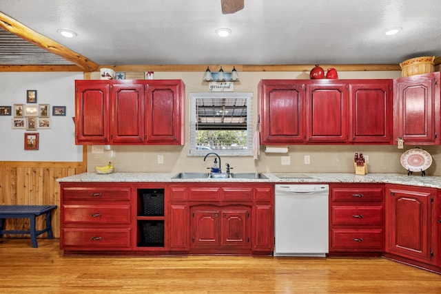 kitchen with white dishwasher, light hardwood / wood-style floors, wood walls, and sink