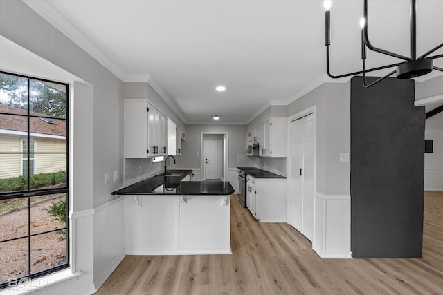 kitchen with kitchen peninsula, light wood-type flooring, backsplash, an inviting chandelier, and white cabinetry