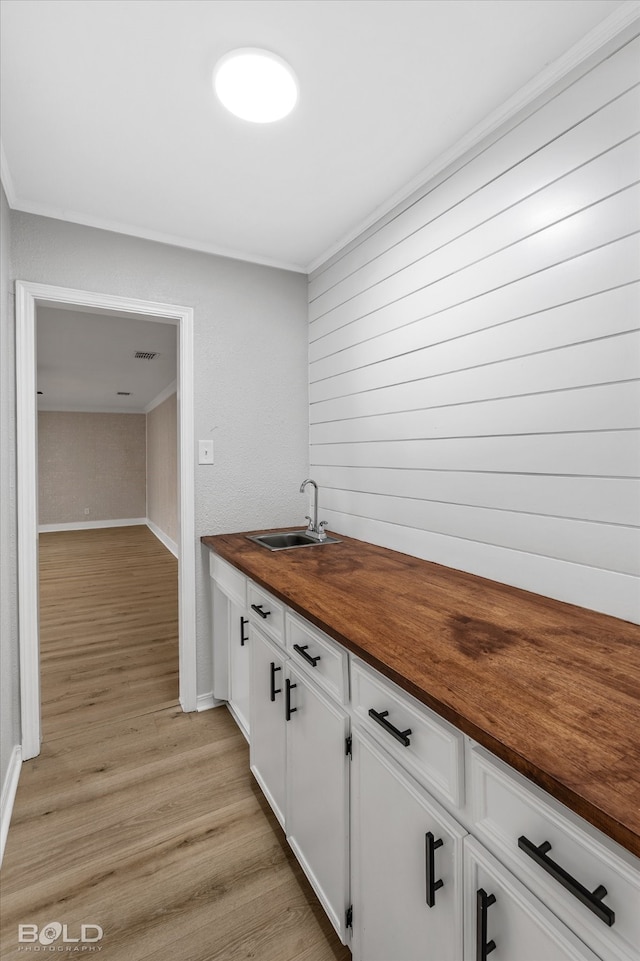 kitchen with white cabinetry, sink, wood counters, light hardwood / wood-style floors, and ornamental molding