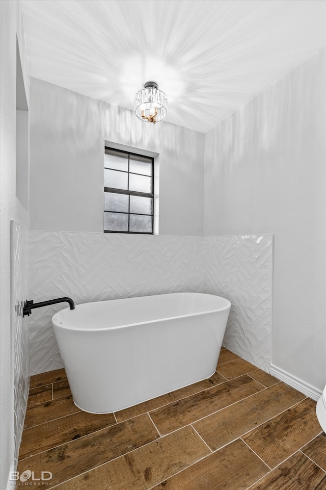 bathroom featuring a bathing tub, a notable chandelier, and tile walls