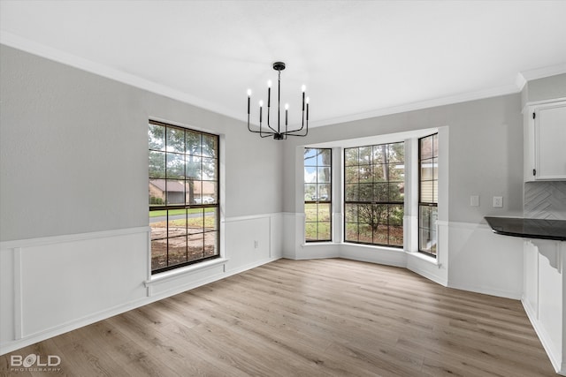 unfurnished dining area with a chandelier, light wood-type flooring, a wealth of natural light, and ornamental molding