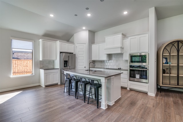 kitchen with appliances with stainless steel finishes, a breakfast bar, a kitchen island with sink, sink, and white cabinetry