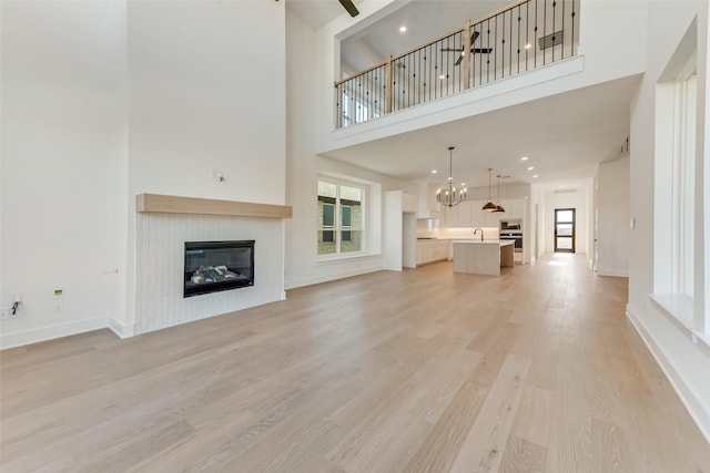 unfurnished living room with light wood-type flooring, a towering ceiling, plenty of natural light, and sink