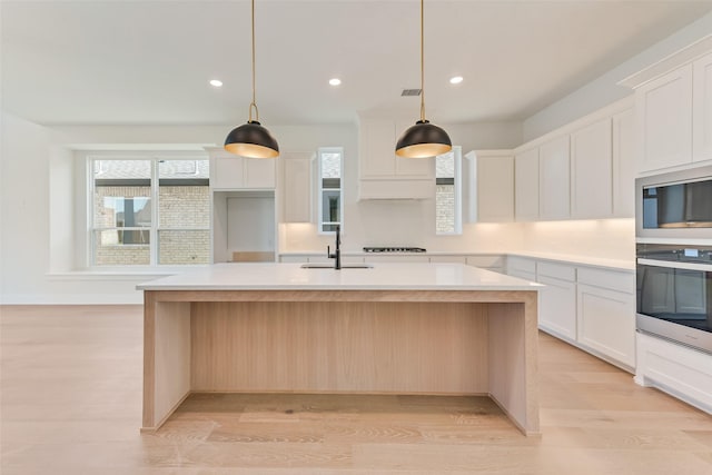 kitchen with a center island with sink, white cabinets, pendant lighting, and light wood-type flooring