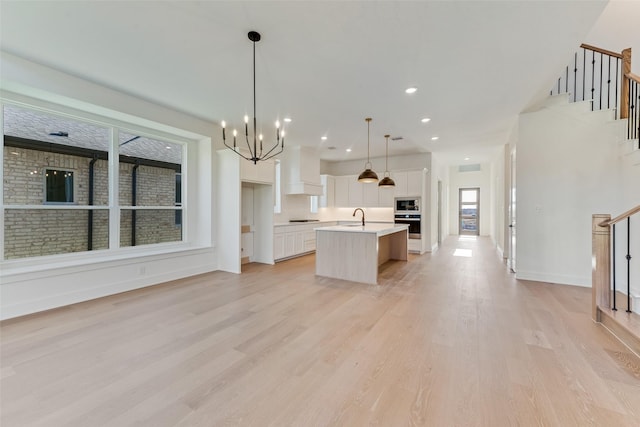 kitchen featuring white cabinetry, built in microwave, sink, pendant lighting, and a kitchen island with sink