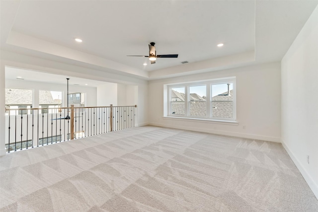 empty room featuring light colored carpet, a raised ceiling, and ceiling fan