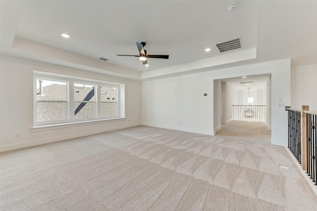 unfurnished living room with light colored carpet, a raised ceiling, and ceiling fan