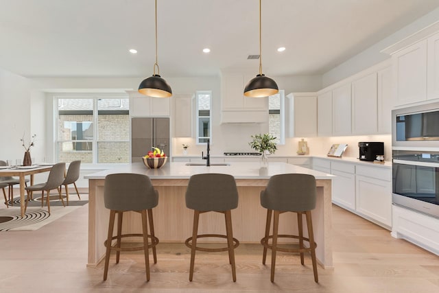 kitchen featuring white cabinets, a kitchen island with sink, and hanging light fixtures