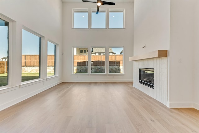 unfurnished living room featuring a tile fireplace, ceiling fan, light hardwood / wood-style flooring, and a high ceiling