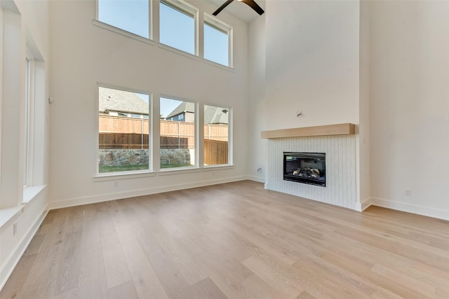 unfurnished living room featuring ceiling fan, light hardwood / wood-style flooring, and a towering ceiling