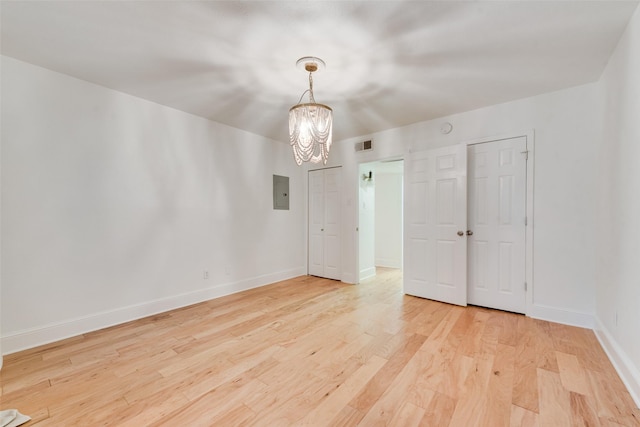 unfurnished room with electric panel, light wood-type flooring, and a notable chandelier