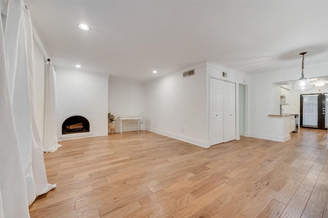 unfurnished living room with a large fireplace, light wood-type flooring, and ornamental molding