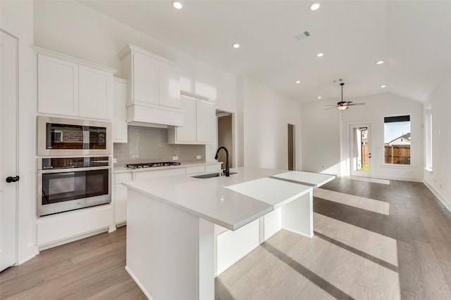 kitchen with appliances with stainless steel finishes, a kitchen island with sink, ceiling fan, light hardwood / wood-style flooring, and white cabinetry