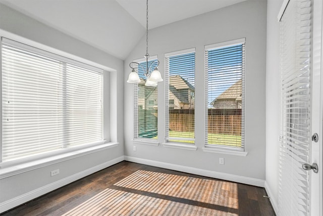 unfurnished dining area with dark wood-type flooring, lofted ceiling, a chandelier, and baseboards