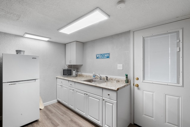 kitchen with sink, light hardwood / wood-style flooring, white fridge, a textured ceiling, and white cabinets