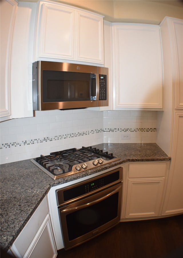 kitchen featuring white cabinets, appliances with stainless steel finishes, backsplash, and dark stone countertops