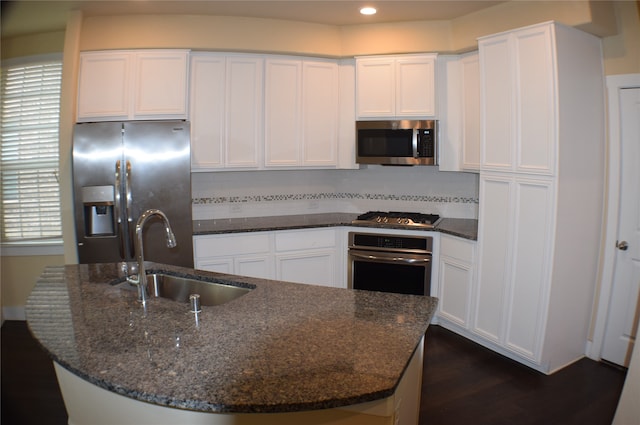 kitchen with white cabinets, stainless steel appliances, dark stone countertops, and sink