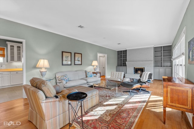 living room with crown molding, built in features, a fireplace, and light hardwood / wood-style flooring