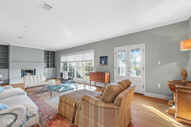 living room with french doors, crown molding, a brick fireplace, built in features, and light wood-type flooring