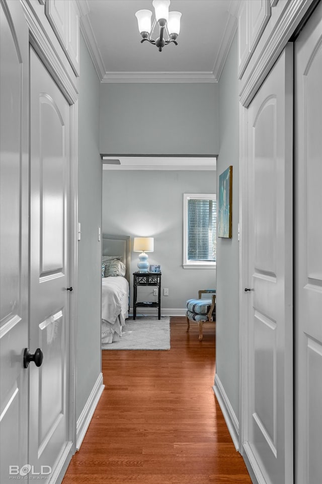 corridor with crown molding, wood-type flooring, and a notable chandelier