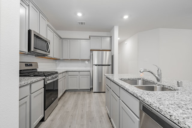 kitchen featuring light stone countertops, sink, light hardwood / wood-style flooring, decorative backsplash, and appliances with stainless steel finishes