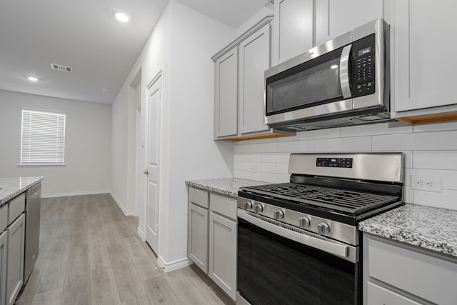 kitchen featuring light stone counters, light hardwood / wood-style flooring, backsplash, gray cabinets, and appliances with stainless steel finishes