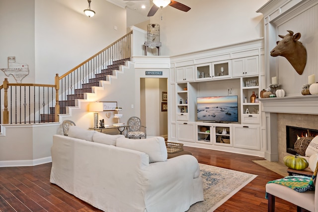 living room with dark hardwood / wood-style flooring, a towering ceiling, ceiling fan, and a tiled fireplace