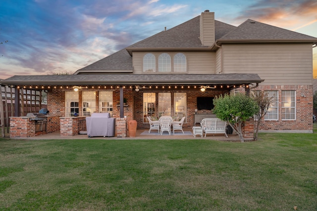 back house at dusk with a lawn, area for grilling, and a patio area