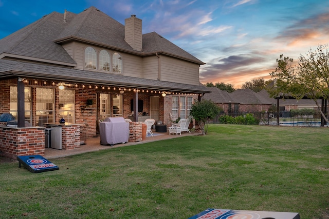 back house at dusk featuring a lawn, exterior kitchen, and a patio