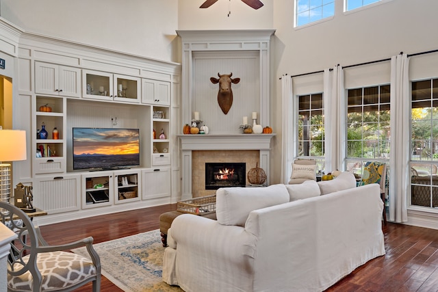 living room with a fireplace, a high ceiling, ceiling fan, and dark wood-type flooring