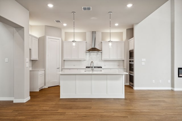 kitchen featuring white cabinetry, an island with sink, wall chimney range hood, and light wood-type flooring