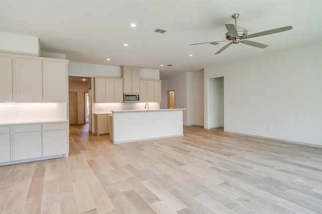 kitchen featuring backsplash, ceiling fan, an island with sink, and light wood-type flooring