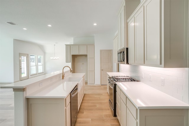 kitchen featuring light wood-type flooring, stainless steel appliances, sink, white cabinetry, and hanging light fixtures