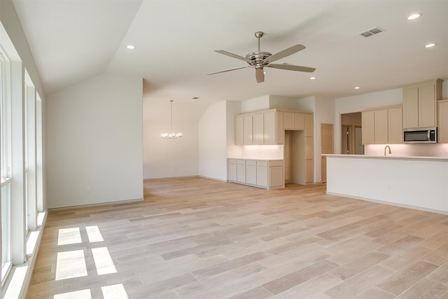 unfurnished living room with ceiling fan with notable chandelier, light wood-type flooring, and vaulted ceiling