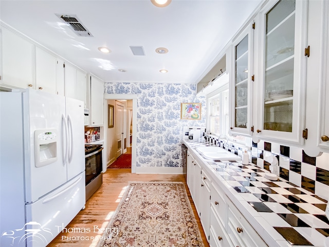 kitchen with white cabinetry, sink, light hardwood / wood-style flooring, white refrigerator with ice dispenser, and stainless steel electric stove