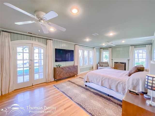 bedroom featuring french doors, light wood-type flooring, access to outside, ceiling fan, and a fireplace