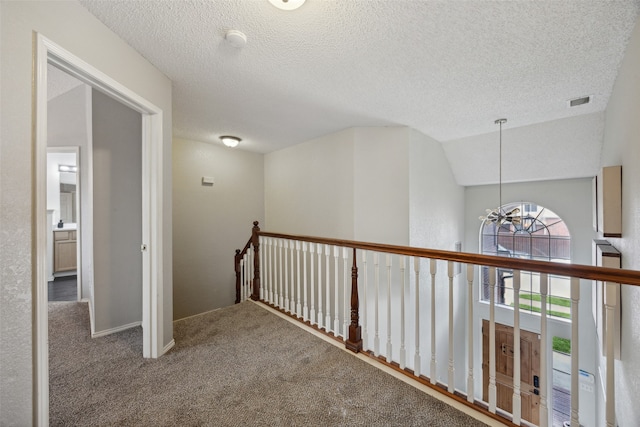 corridor with carpet, a textured ceiling, lofted ceiling, and a notable chandelier