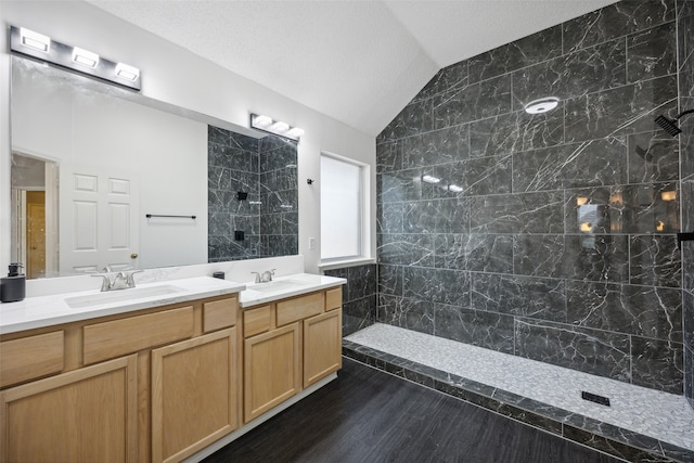 bathroom featuring vanity, lofted ceiling, a textured ceiling, tiled shower, and wood-type flooring