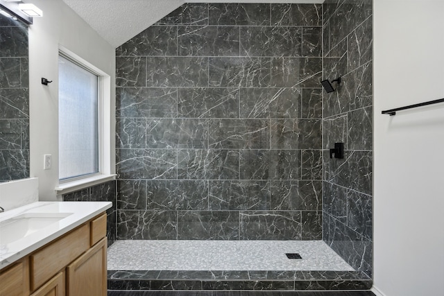 bathroom with vanity, a tile shower, a textured ceiling, and plenty of natural light