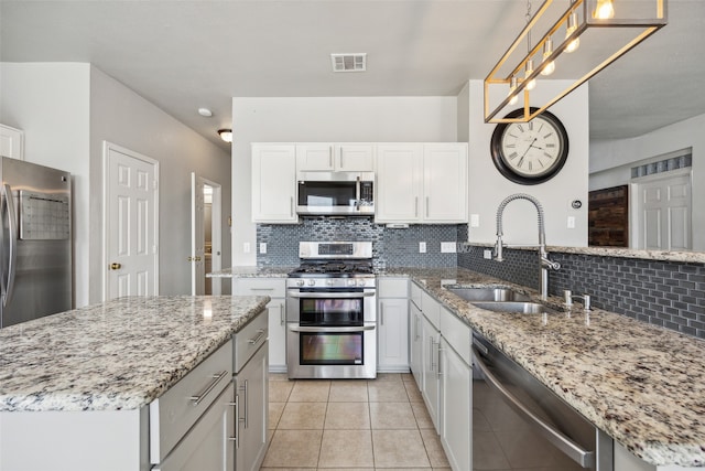 kitchen featuring light stone countertops, stainless steel appliances, sink, pendant lighting, and white cabinetry