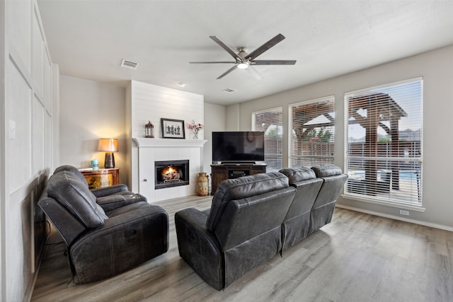 living room featuring light hardwood / wood-style floors, ceiling fan, and a tiled fireplace